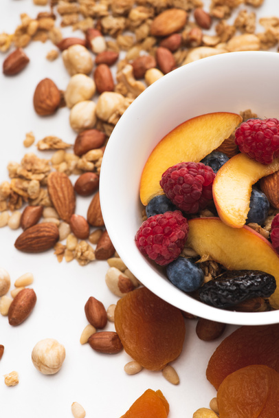 смачна гранола з горіхами, ягодами та фруктами в мисці на білому
 - Фото, зображення