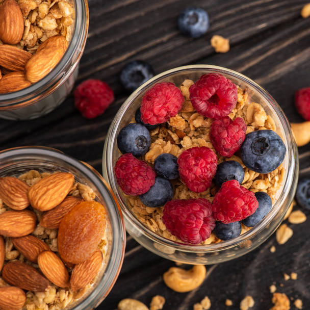 closeup of delicious granola with berries, dried apricots, nuts and yogurt in glass cups on wooden surface - Photo, Image
