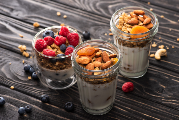 delicious granola with berries, dried apricots, nuts and yogurt in glass cups on wooden surface - Photo, Image