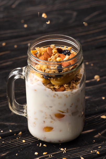 delicious granola with yogurt, nuts, peach, blueberry in glass jar - Фото, изображение