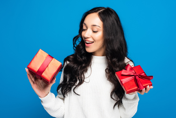 happy woman in sweater looking at christmas gift box isolated on blue - Fotoğraf, Görsel