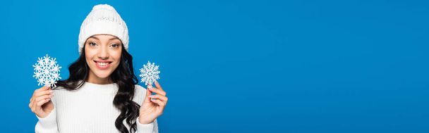 young woman in knitted hat holding decorative snowflakes isolated on blue, banner - Photo, Image