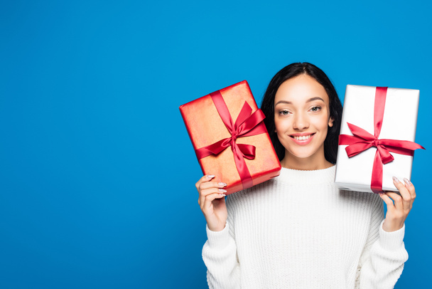 cheerful woman in knitted sweater holding gifts isolated on blue - Foto, Imagem