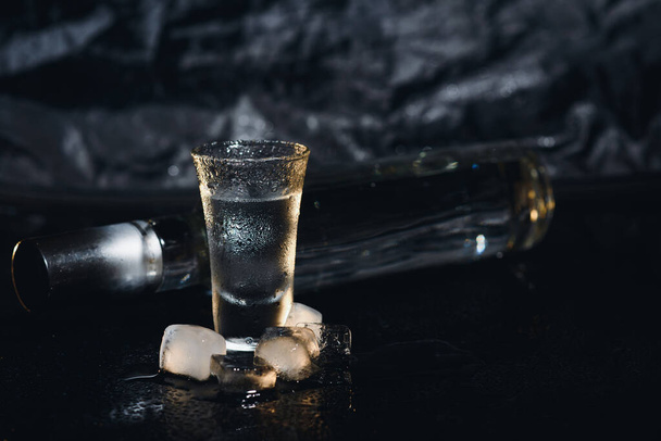 Vodka fekete hátterű feles poharakban, jeges erős ital ködös üvegben - Fotó, kép