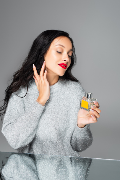 щаслива жінка з червоними губами наносить парфуми ізольовані на сірий
  - Фото, зображення
