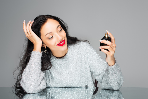 pleased woman with red lips holding bottle with perfume isolated on grey  - Foto, Imagem