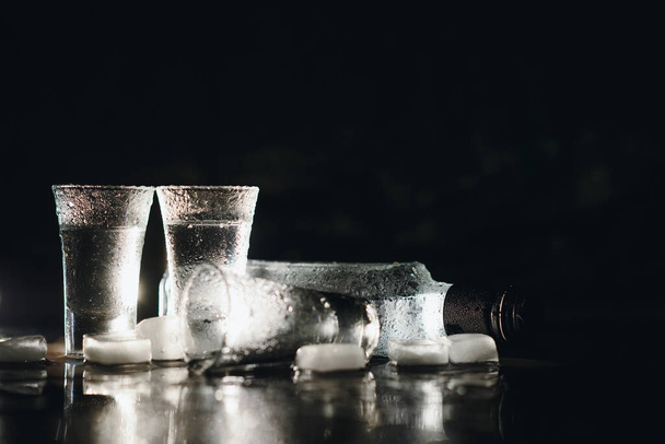 Close-up view of bottle of vodka with glasses standing on ice on black - Fotografie, Obrázek