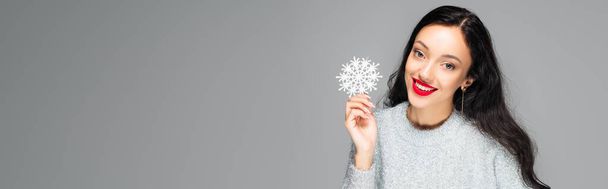 pleased woman with red lips holding decorative snowflake isolated on grey, banner - Photo, Image