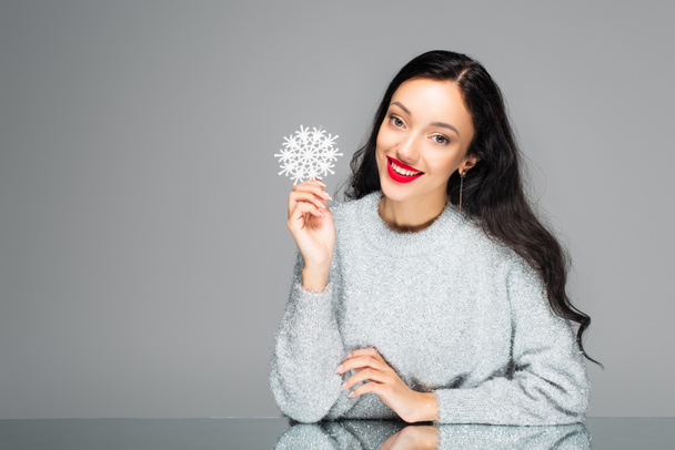pleased young woman with red lips holding decorative snowflake isolated on grey - Valokuva, kuva