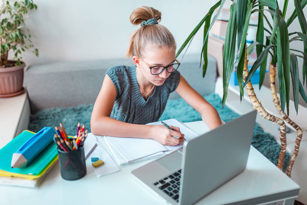 Beautiful young school girl left-handed working at home in her room with laptop and class notes studying in a virtual class. Distance and online education, e-learning during quarantine - Φωτογραφία, εικόνα