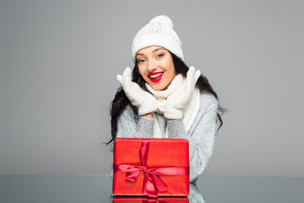 ενθουσιασμένοι γυναίκα στο χειμερινό ντύσιμο κοντά παρούσα απομονώνονται σε γκρι - Φωτογραφία, εικόνα