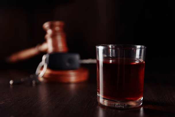 Llave del coche, martillo juez de madera y bebida de alcohol whisky en un vaso en una mesa oscura. No beber y conducir concepto abstracto - Foto, imagen