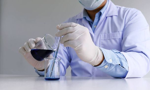 Investigador de laboratorio médico o científico masculino realiza pruebas con líquido azul en el laboratorio. Concepto de equipo de laboratorio y experimentos científicos - Foto, imagen