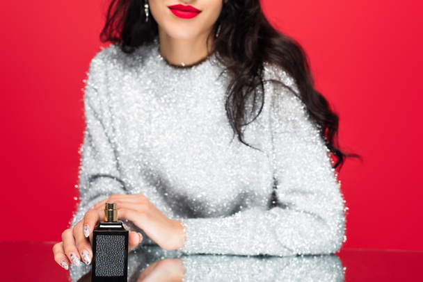 cropped view of brunette woman holding bottle with perfume isolated on red - Φωτογραφία, εικόνα