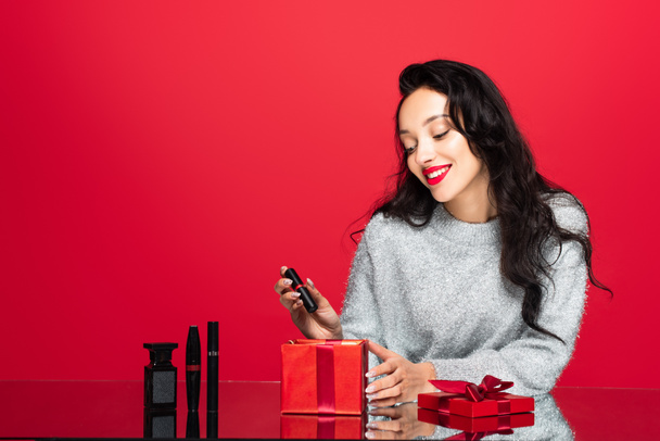happy woman taking lipstick from gift box near decorative cosmetics on red - 写真・画像