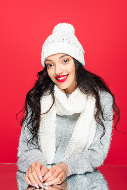 joyful woman in hat and warm scarf isolated on red - Foto, afbeelding