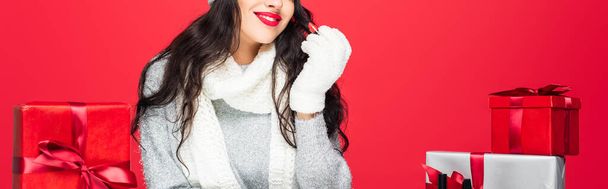 vista ritagliata della donna gioiosa che tiene il rossetto vicino a Natale presenta isolato sul rosso, banner - Foto, immagini