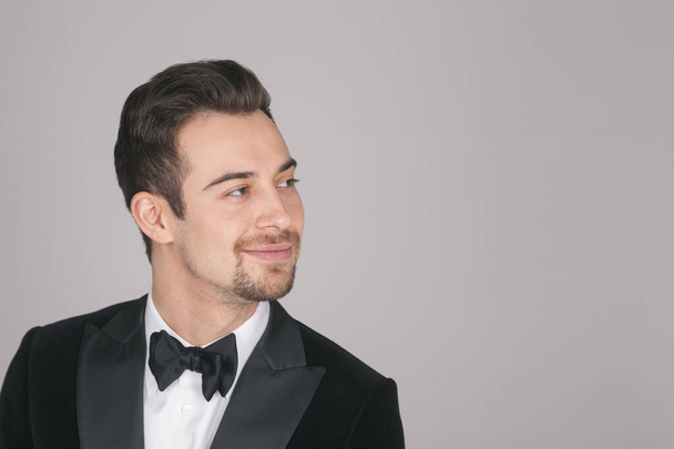 Studio portrait of a young caucasian man in a tuxedo, looking to the side, against plain studio background - Photo, Image