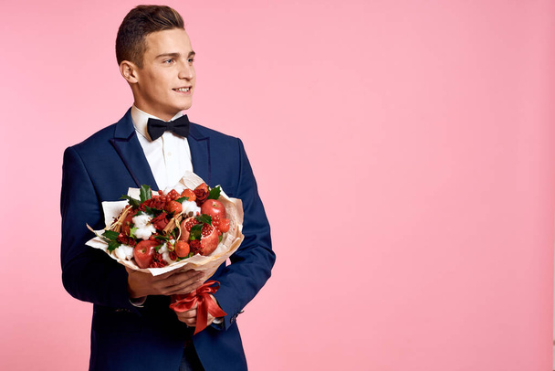 Hombre guapo en un traje clásico con un ramo de flores en un fondo rosa vacaciones lazo modelo - Foto, imagen