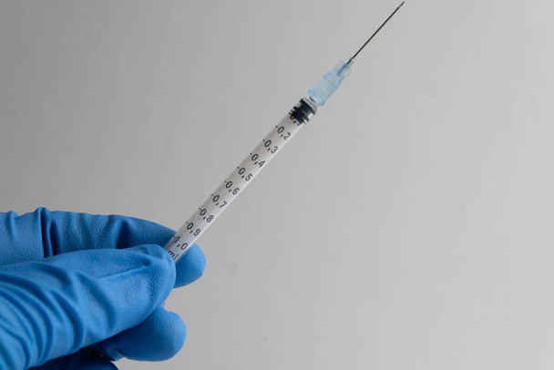 seringa com agulha mantida por uma mão protegida por uma luva azul isolada sobre um fundo branco - Foto, Imagem
