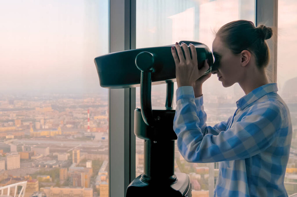 Jonge vrouw op zoek door toeristische telescoop en het verkennen van het stadsgezicht - Foto, afbeelding
