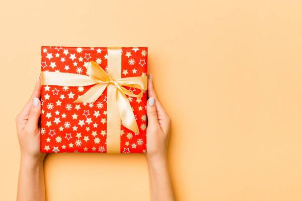 Flat lay of woman hands holding gift wrapped and decorated with bow on gold background with copy space. Christmas and holiday concept. - Φωτογραφία, εικόνα