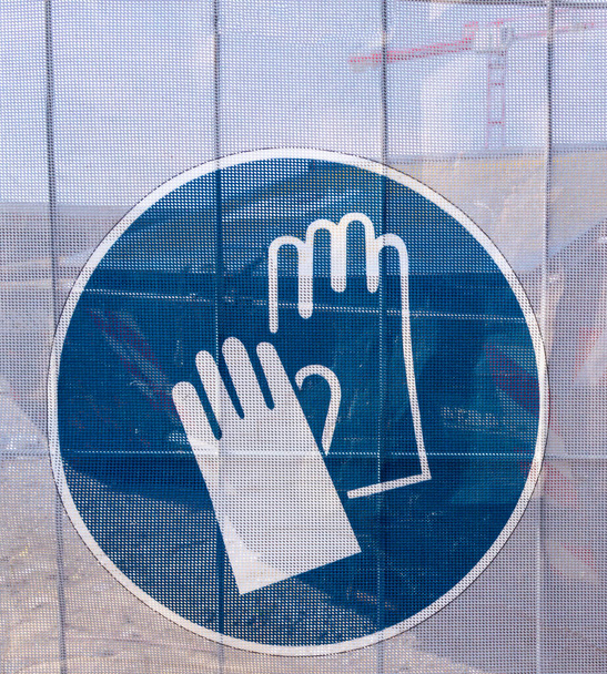 Symbole sur une bâche transparente, à travers laquelle des parties du chantier sont vues, comme une indication de sécurité sur un chantier de construction. Vous pouvez voir que vous devriez porter des gants de travail.  - Photo, image