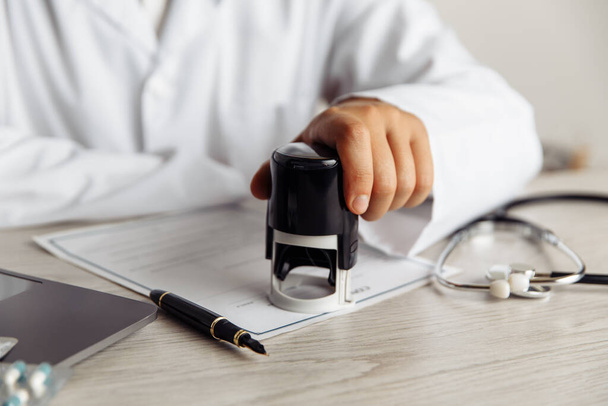 Male doctor in public medical office is stamping medical document. Healthcare and medicine concept - Photo, Image