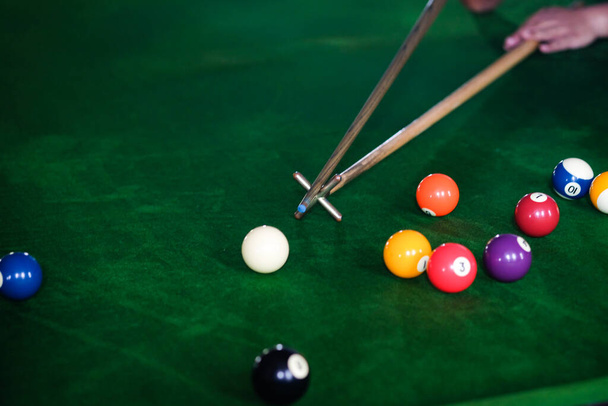 Man's hand and Cue arm playing snooker game or preparing aiming to shoot pool balls on a green billiard table. Colorful snooker balls on green frieze - Photo, Image