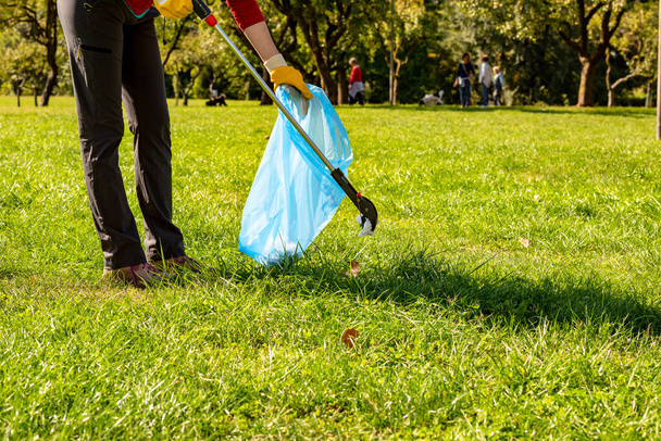 Vrijwillige vrouw met gele handschoenen en grijper die vuilnis opruimt voor schoonmaak in het park. Ecologisch concept - Foto, afbeelding
