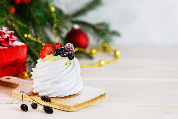 Dessert Pavlova on a wooden board against the background of the Christmas tree. Horizontal orientation, copy space. - Zdjęcie, obraz