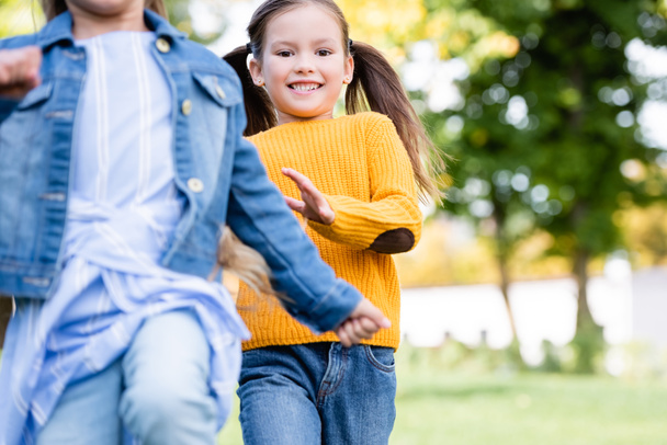 Veselý dívka běží v blízkosti přítele na rozmazané popředí v parku  - Fotografie, Obrázek