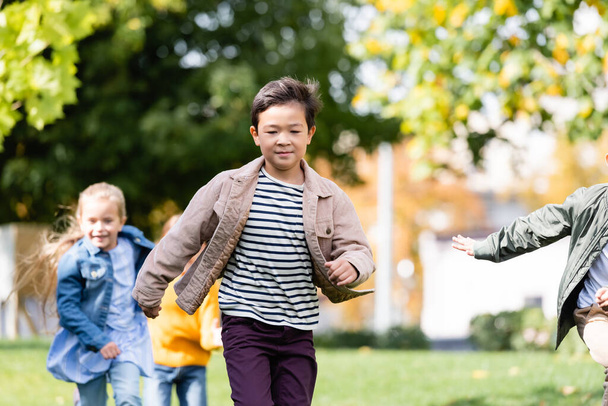 Ázsiai fiú fut közel barátok elmosódott háttér a parkban  - Fotó, kép