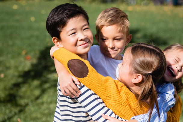 Asian boy looking at camera while hugging smiling friends outdoors  - Foto, imagen