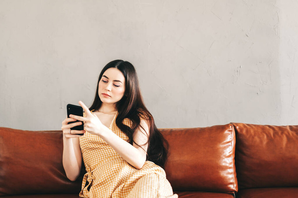 Young caucasian woman using smartphone while resting on a stylish sofa at home. High quality photo - Zdjęcie, obraz