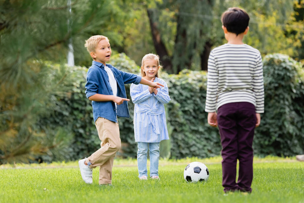 Excited boy pointing with fingers near football and friends in park  - Foto, Imagem
