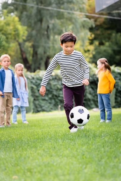Asian boy playing football near friends in park at background  - Foto, Imagen