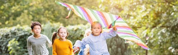Girl with flying kite running near multiethnic friends in park, banner  - Photo, Image