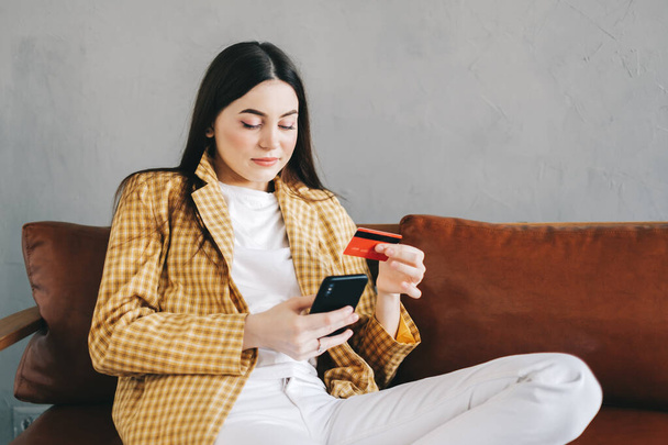 Young caucasian woman holding credit card, using smartphone and shopping online. E-commerce, internet banking, spending money. High quality photo - Photo, Image