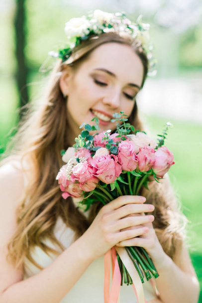 The bride in white wedding dress is holding a bouquet in green park. Summer wedding on a sunny day. - Foto, Imagem