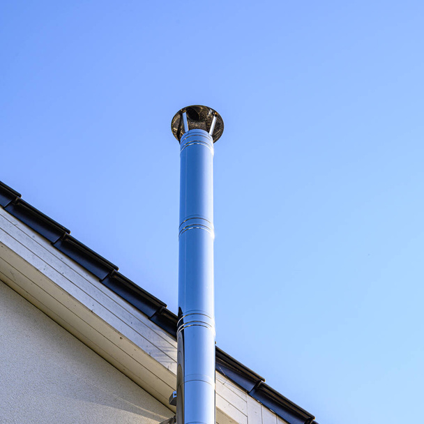 Ruostumattomasta teräksestä valmistettu savupiippu ja osat katosta kirkkaan sinisen taivaan edessä. - Valokuva, kuva