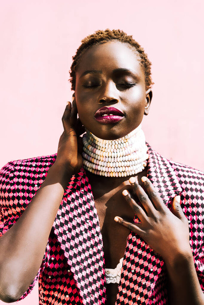 ピンクを背景に黒い肌の美しいアフリカのモデル。本物の笑顔だ。鮮やかな色、キャンディーネックレス。高品質の写真 - 写真・画像