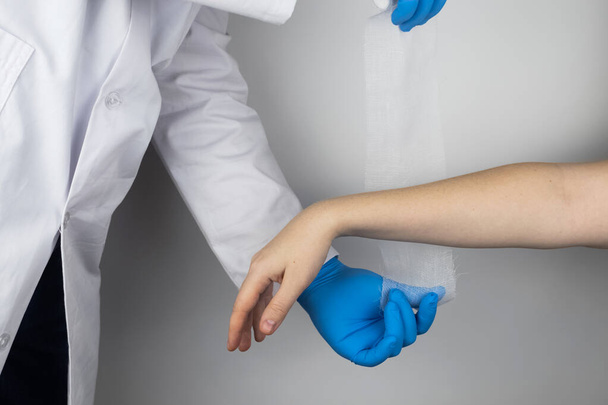The traumatologist puts a bandage on the forearm of the female patient. The concept of help with fractures and sprains. The technique of applying a cruciform bandage. - 写真・画像