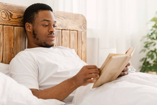 Black Man Enjoying Reading Book Lying In Bed At Home - Foto, imagen