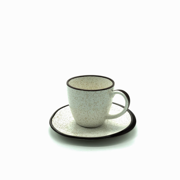 Bej porselen bardak ve küçük kahverengi noktalı ve jantlı çay tabağı. Yan görüş. Beyaz arkaplan üzerinde izole edilmiş. - Fotoğraf, Görsel