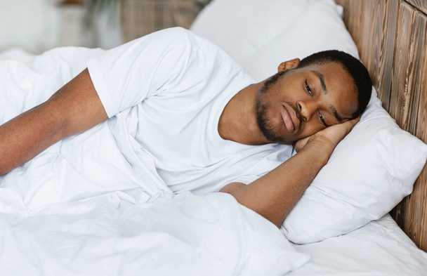 Θλιβερός μαύρος ξαπλωμένος έχοντας αϋπνία στο υπνοδωμάτιο στο σπίτι - Φωτογραφία, εικόνα