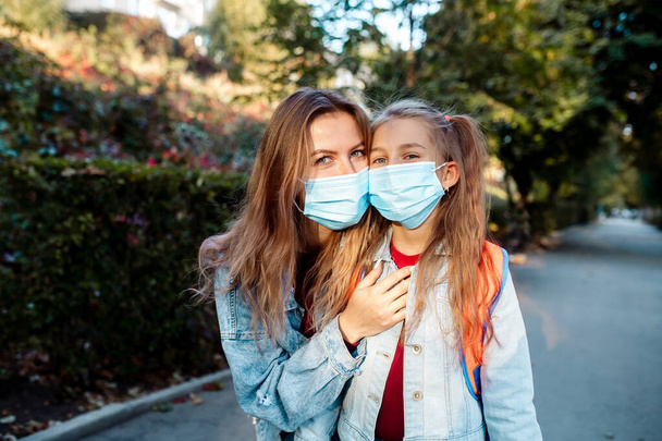 Back to school. In the fall, a 7-year-old girl, together with a young mother of the family, goes to school wearing face masks. - Foto, imagen