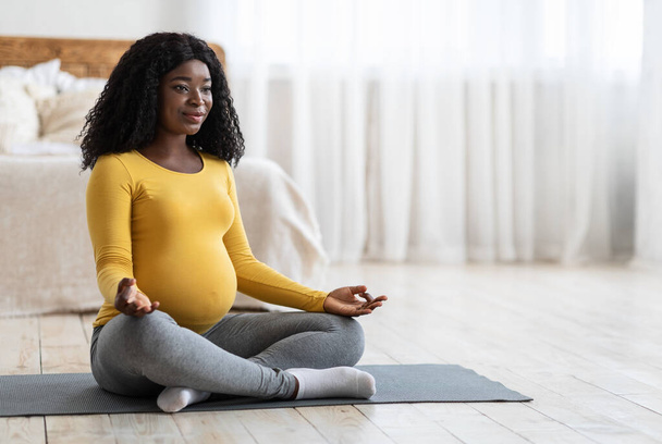Pregnant african woman meditating in lotus position at home - Photo, Image