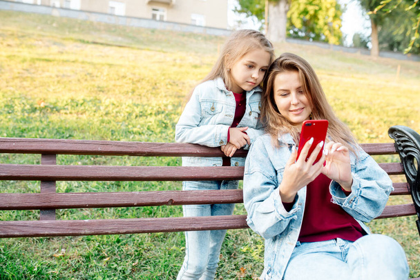 A young mother and her daughter 7 years old are talking on an online connection on a walk in the park - Fotoğraf, Görsel
