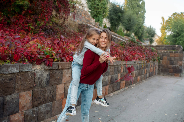 Beautiful young family mom hugs her pretty daughter on a walk in the park in autumn - Zdjęcie, obraz